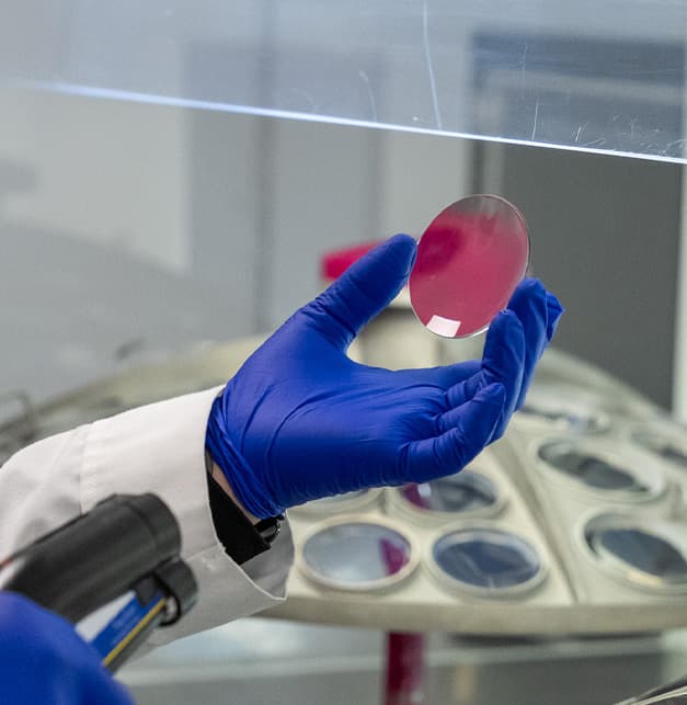 A gloved technician holding up a lens in the lab