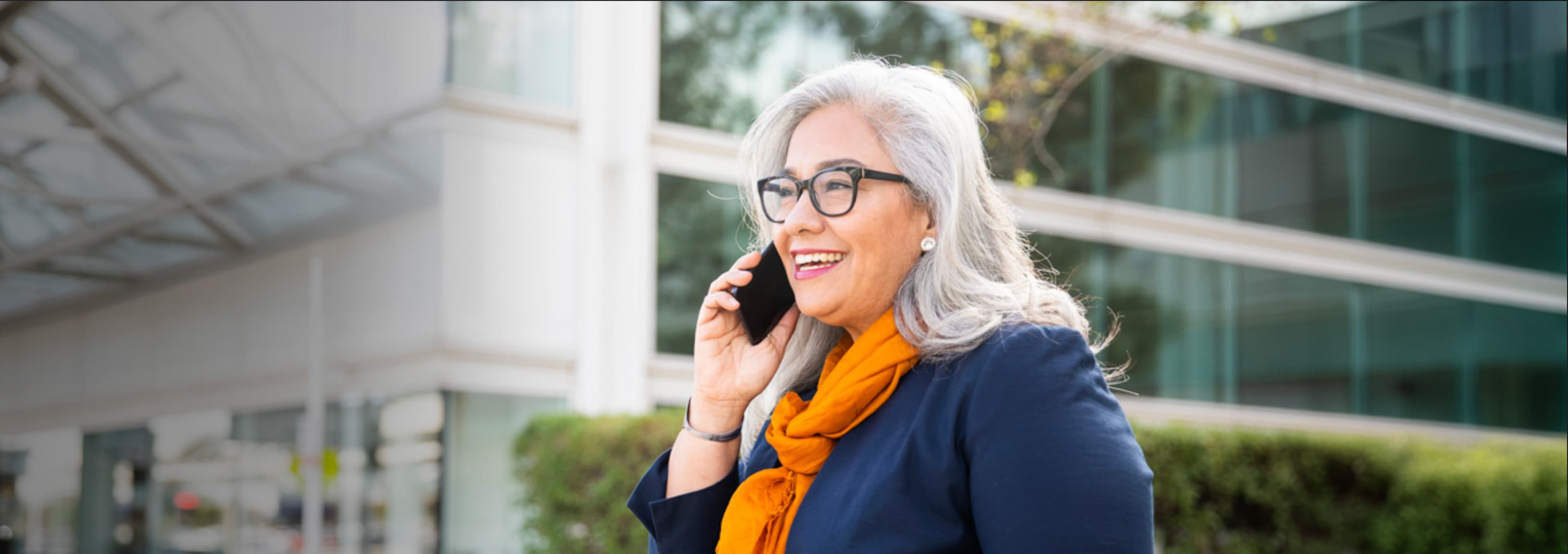 A woman in glasses talking on her phone outside an office building