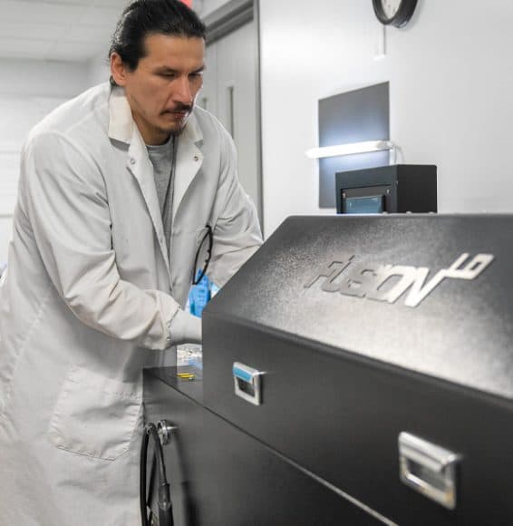 A technician running lenses through coating equipment at EyeKraft